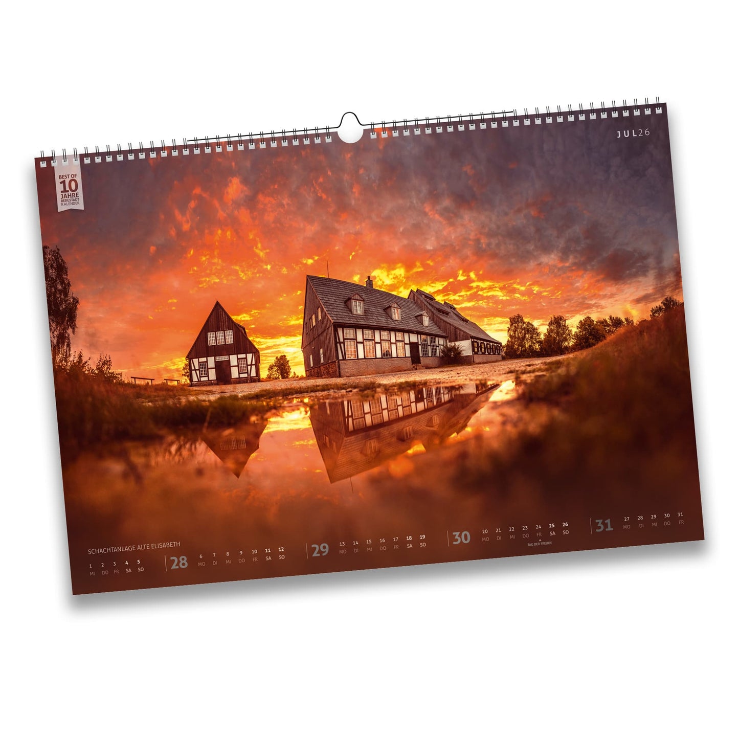 Juli-Motiv des Bergstadtkalenders 2026: Schachtanlage Alte Elisabeth in Freiberg bei Sonnenaufgang, mit leuchtendem Himmel und Spiegelung in einer Pfütze.