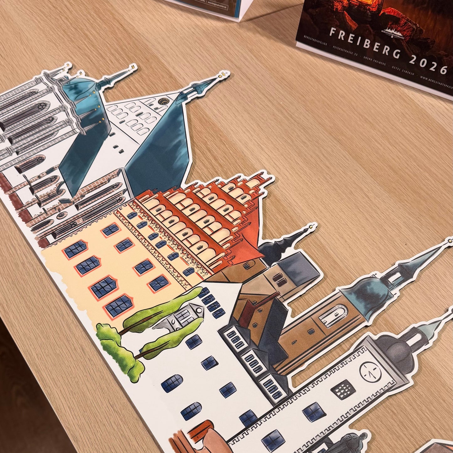 Illustrative Stadtsilhouette von Freiberg aus konturgefrästem Alu-Dibond, detailreiche Gebäudeansicht auf Holztisch.