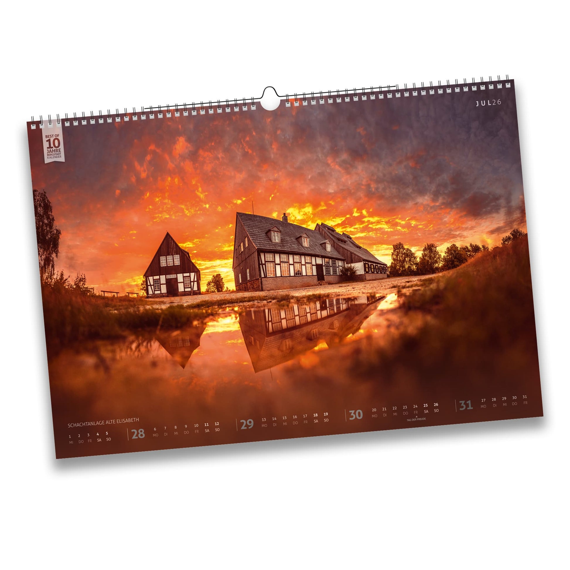 Juli-Motiv des Bergstadtkalenders 2026: Schachtanlage Alte Elisabeth in Freiberg bei Sonnenaufgang, mit leuchtendem Himmel und Spiegelung in einer Pfütze.