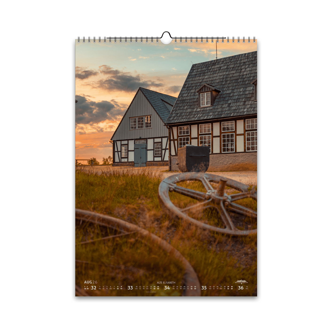 August-Motiv des Bergstadtkalenders 2026 im DIN-A3-Hochformat: die Alte Elisabeth in Freiberg bei Sonnenuntergang, mit Schwarzenberggebläse und Betstube und alten Seilscheiben im Vordergrund.