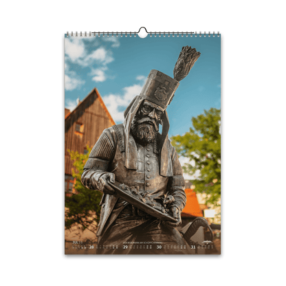 Juli-Motiv des Bergstadtkalenders 2026 im DIN-A3-Hochformat: die detailreiche Bergmann-Figur des Silberwegs am Schüppchenberg in Freiberg, im warmen Sommerlicht vor historischen Gebäuden.