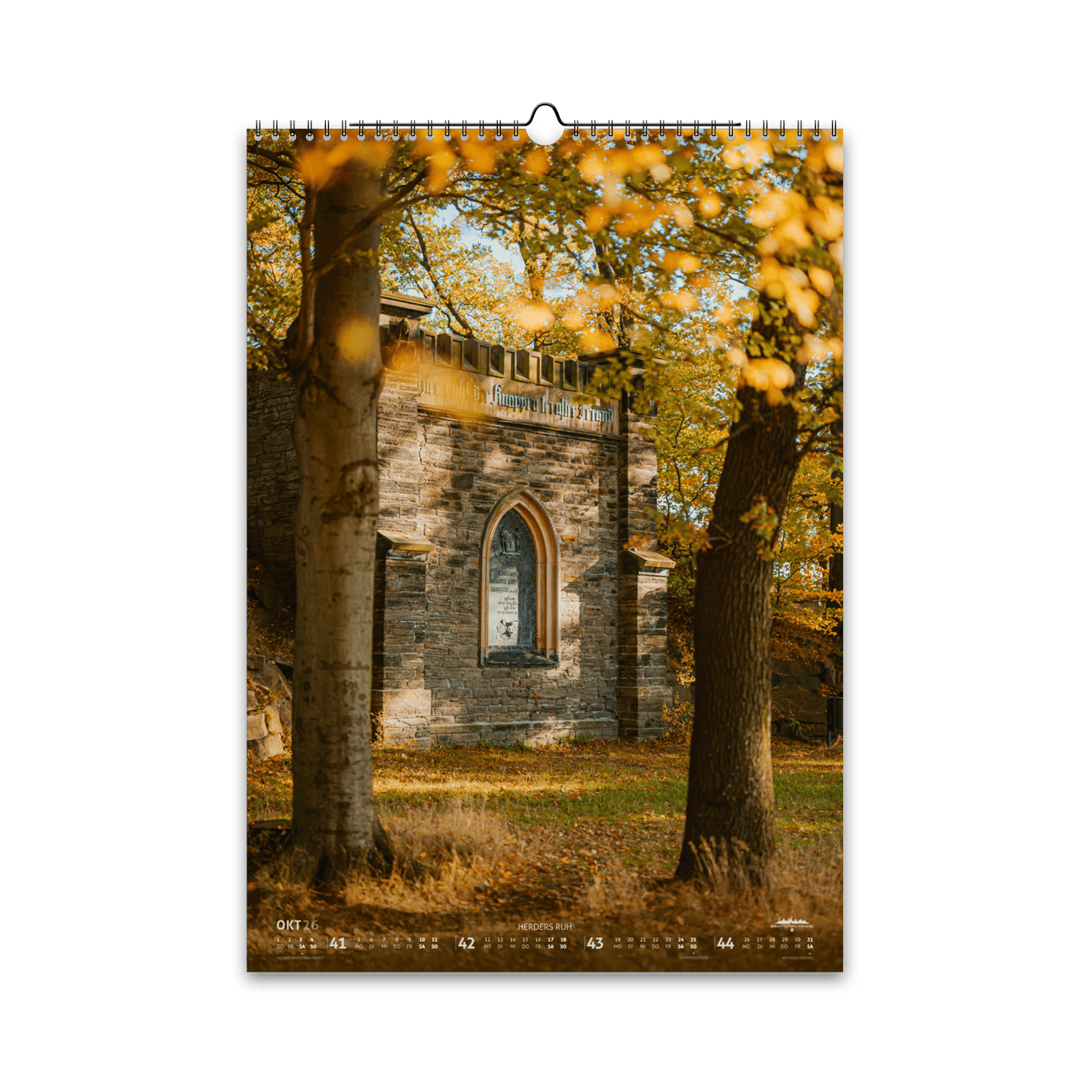 Oktober-Motiv des Bergstadtkalenders 2026 im DIN-A3-Hochformat: das historische Grabstätte Herders Ruh in Freiberg, umgeben von goldenem Herbstlaub und warmem Sonnenlicht zwischen den Bäumen.