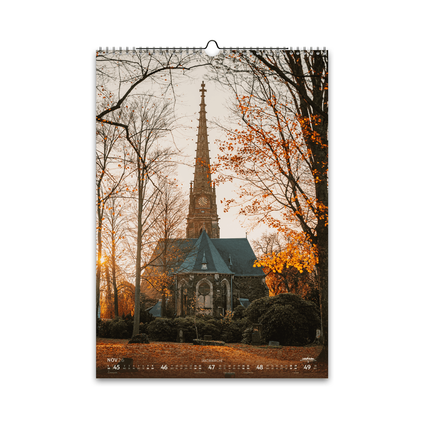November-Motiv des Bergstadtkalenders 2026 im DIN-A3-Hochformat: die Jakobikirche aus sicht des Donatsfriedhofs in Freiberg im sanften Licht des Spätherbstes, umgeben von kahlen Bäumen und goldenem Laub.