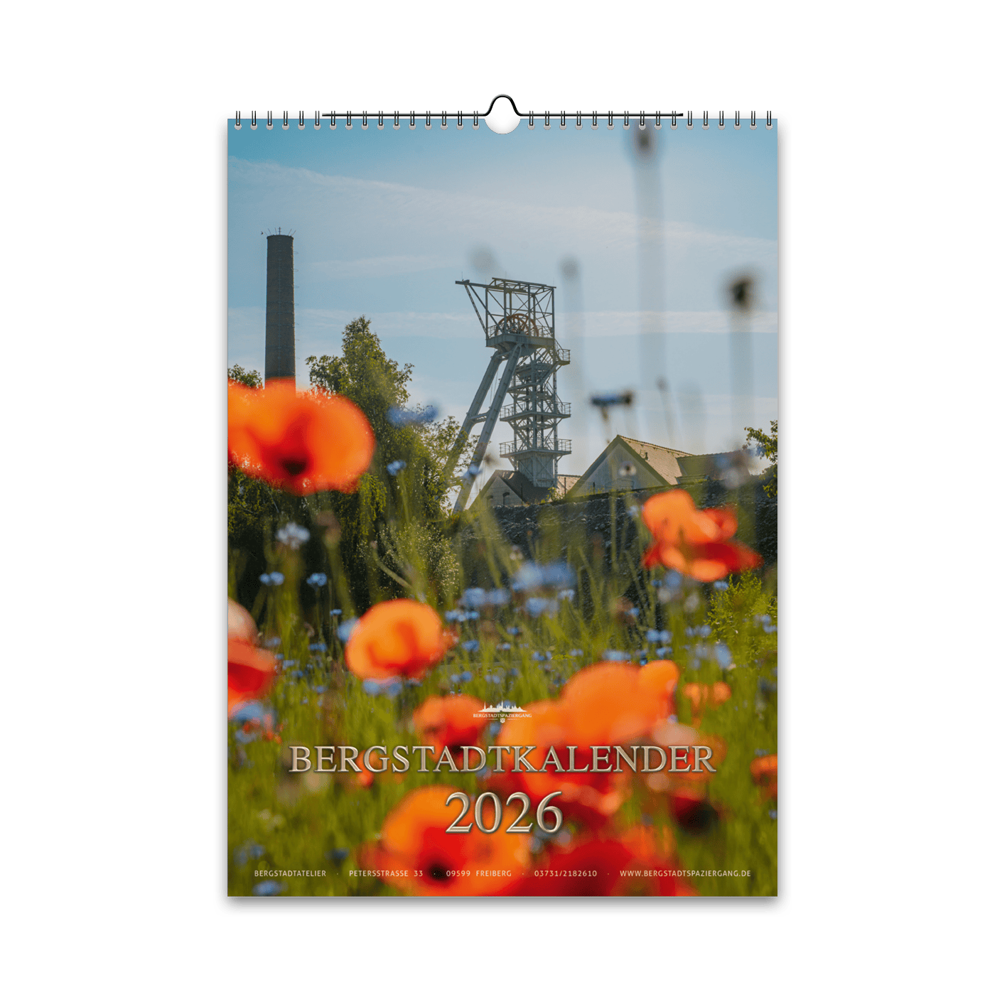 Titelmotiv des Bergstadtkalenders 2026 im DIN-A3-Hochformat mit dem Förderturm der Reichen Zeche in Freiberg, umgeben von leuchtenden Mohn- und Kornblumen.