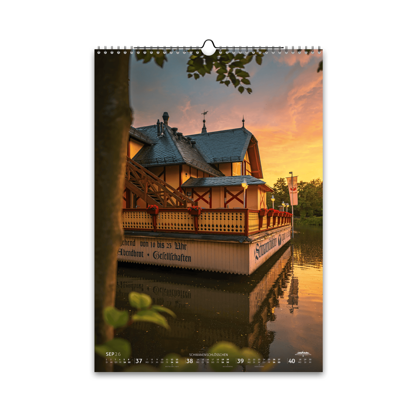 September-Motiv des Bergstadtkalenders 2026 im DIN-A3-Hochformat: das Schwanenschlösschen in Freiberg im goldenen Abendlicht, mit Spiegelung im ruhigen Wasser des Kreuzteichs.