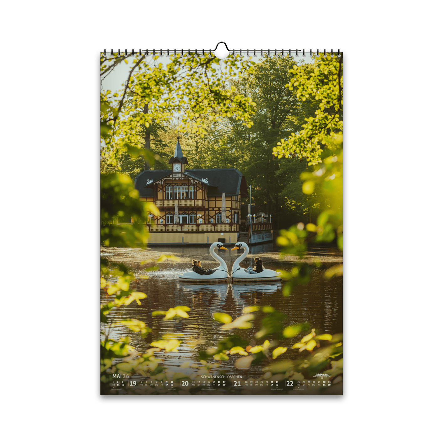 Mai-Motiv des Bergstadtkalenders 2026 im DIN-A3-Hochformat: das Schwanenschlösschen am Kreuzteich in Freiberg, im goldenen Morgenlicht mit zwei arrangierten Schwanenbooten auf dem Wasser.