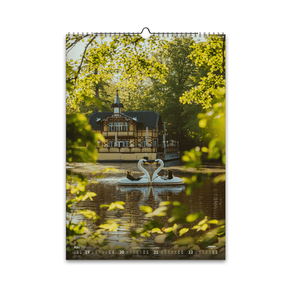 Mai-Motiv des Bergstadtkalenders 2026 im DIN-A3-Hochformat: das Schwanenschlösschen am Kreuzteich in Freiberg, im goldenen Morgenlicht mit zwei arrangierten Schwanenbooten auf dem Wasser.