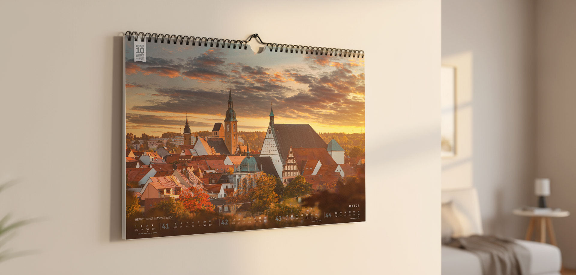 Der Bergstadtkalender 2026 im DIN-B3-Querformat hängt an einer hellen Wohnzimmerwand, umgeben von sanftem Tageslicht – das Bild zeigt, wie der Kalender in einer echten Wohnumgebung wirkt.