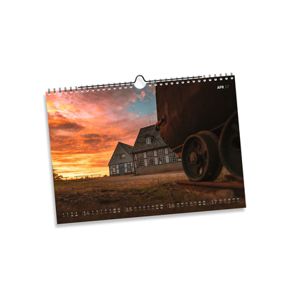 April 2027: Schachtanlage Alte Elisabeth in Freiberg bei orangefarbenem Sonnenuntergang, mit historischem Rad im Vordergrund.