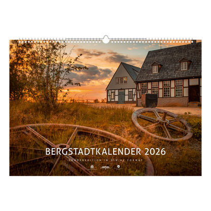 Titelblatt des Bergstadtkalenders 2026 im Sonderformat mit der Alten Elisabeth in Freiberg im warmen Licht des Sonnenuntergangs – historische Bergwerksgebäude mit Seilscheiben im Vordergrund.