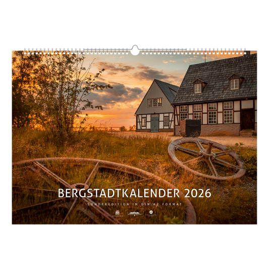 Titelblatt des Bergstadtkalenders 2026 im Sonderformat mit der Alten Elisabeth in Freiberg im warmen Licht des Sonnenuntergangs – historische Bergwerksgebäude mit Seilscheiben im Vordergrund.