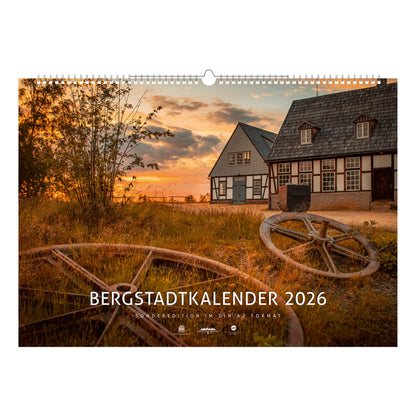Titelblatt des Bergstadtkalenders 2026 im Sonderformat mit der Alten Elisabeth in Freiberg im warmen Licht des Sonnenuntergangs – historische Bergwerksgebäude mit Seilscheiben im Vordergrund.