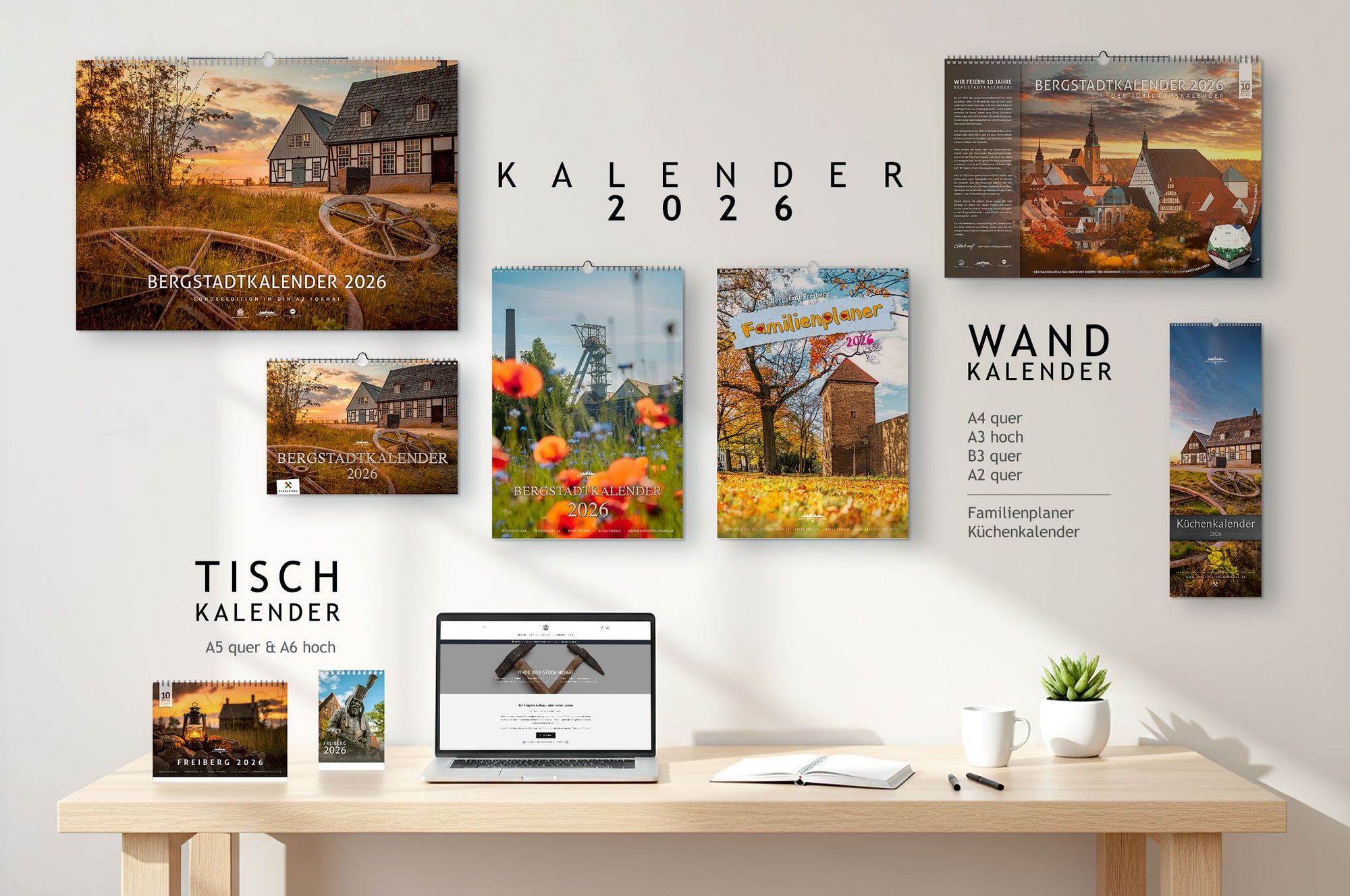 Präsentationsbild des Bergstadtatelier-Kalender-Lineups 2026: an der Wand hängen Wandkalender in verschiedenen Formaten (A4, A3, B3, A2), der Familienplaner und der Küchenkalender. Auf dem Tisch stehen Tischkalender in A5 und A6 sowie ein Laptop mit der Shop-Webseite. Das Bild zeigt das vollständige Sortiment der Kalenderkollektion 2026 in einem modernen, hellen Raum.