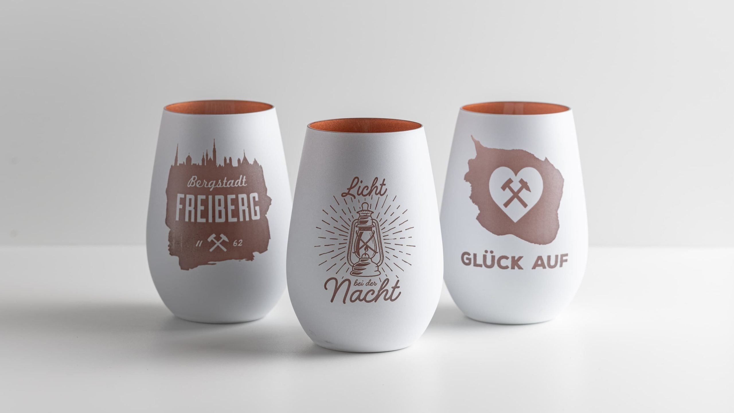 Drei Windlichter aus Glas in Weiß und Bronze mit regionalen Motiven: „Bergstadt Freiberg Skyline“, „Licht bei der Nacht“ und „Glück auf“. Handgefertigt im Bergstadtatelier Freiberg.